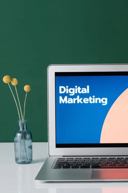 Un espace de travail contemporain où des mains examinent des données marketing sur un ordinateur portable et des documents papier.